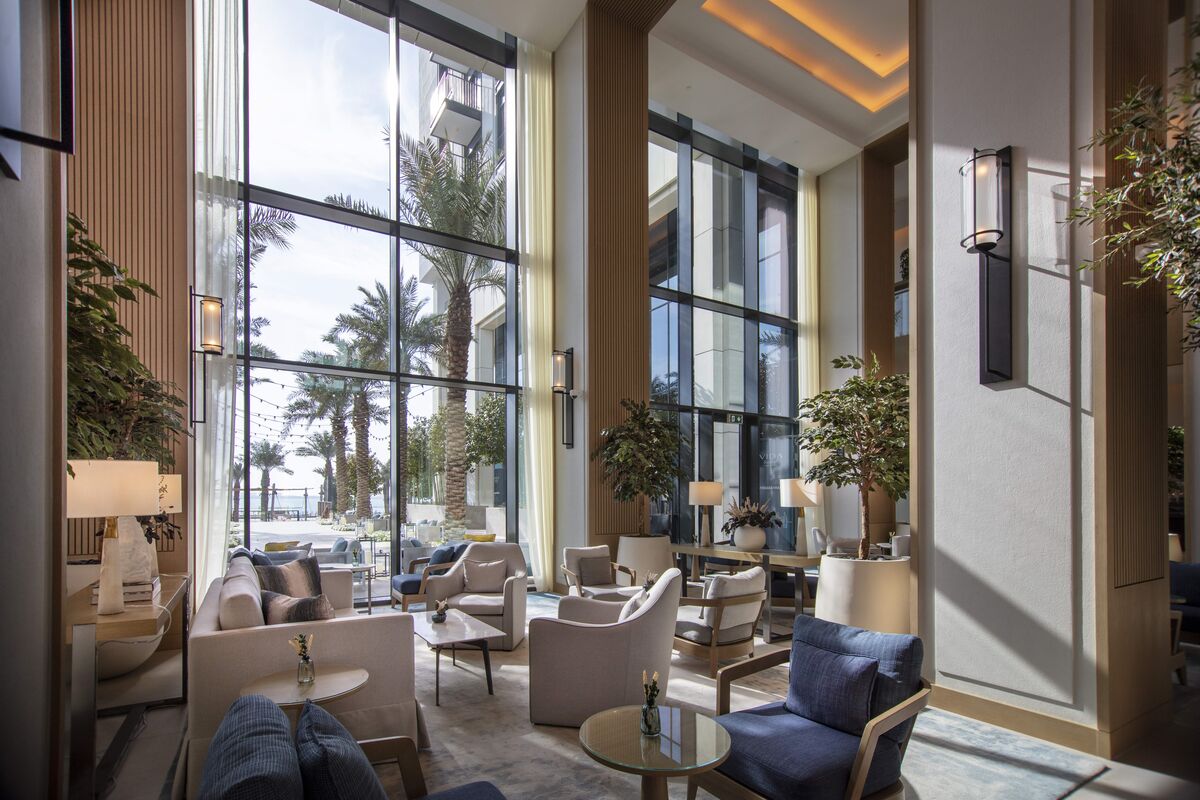 Luxurious hotel lobby with large glass façade, looking out on garden with palm trees.