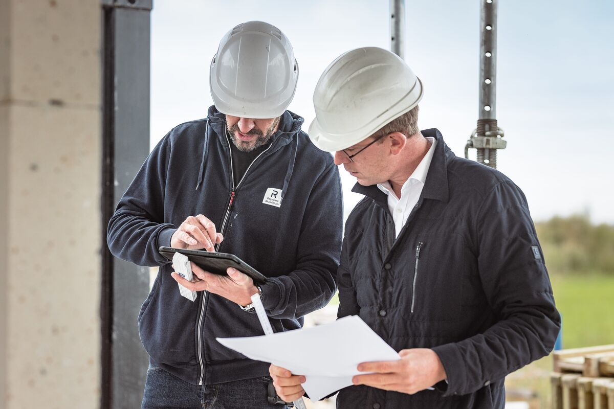 Two people in hard hats looking at tablet and building plans at construction site.