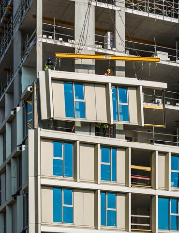 Prefab façade with window being lifted to high-rise building under construction.