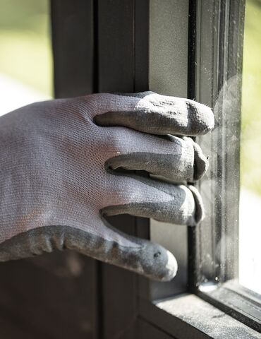 Gloved hand toucing black aluminium window profile on site.